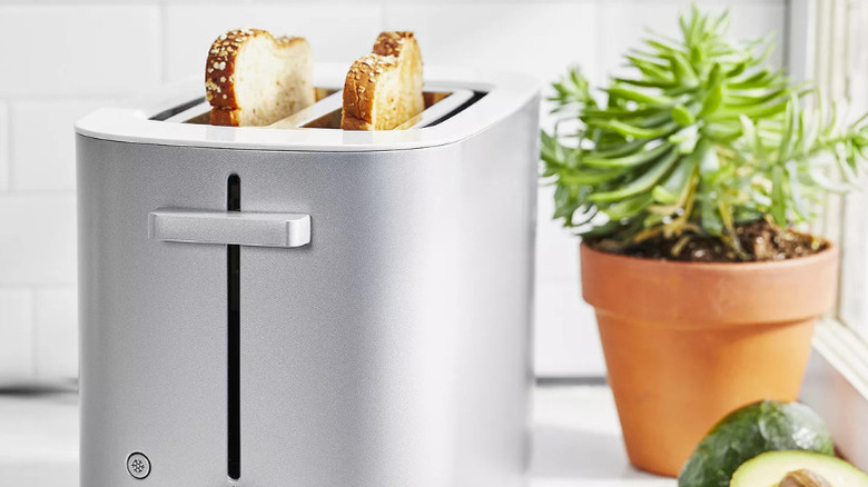 A silver toaster with two toasted slices of bread peeking out of the top