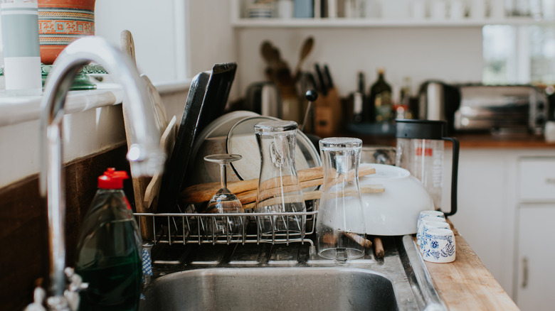 Dish rack in kitchen piled with glassware, utensils, and plates.