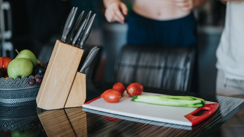 Knives in a knife block with a chopping board with vegetables on it