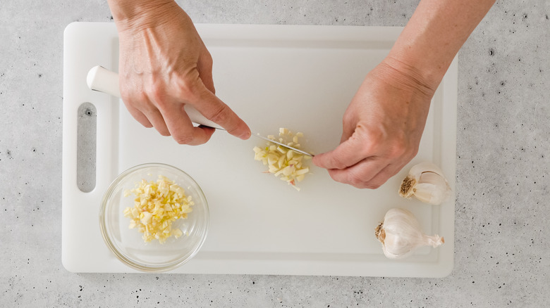 Garlic being chopped on a plastic cutting board