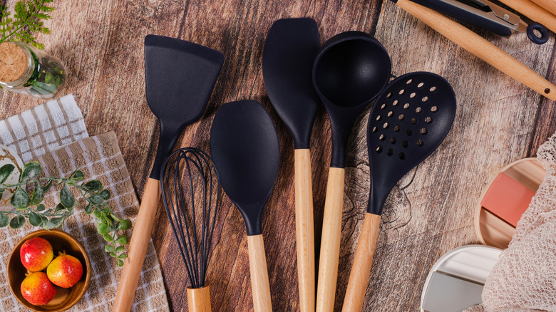 Black plastic spatulas and utensils on wood kitchen table.