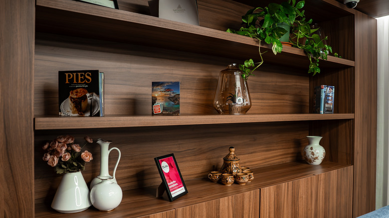 A walnut shelving unit with ornaments, plants, photos and a book on it.