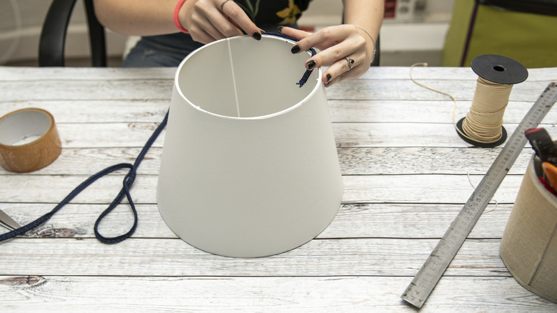 A woman sitting at a desk making a plain ivory lampshade.