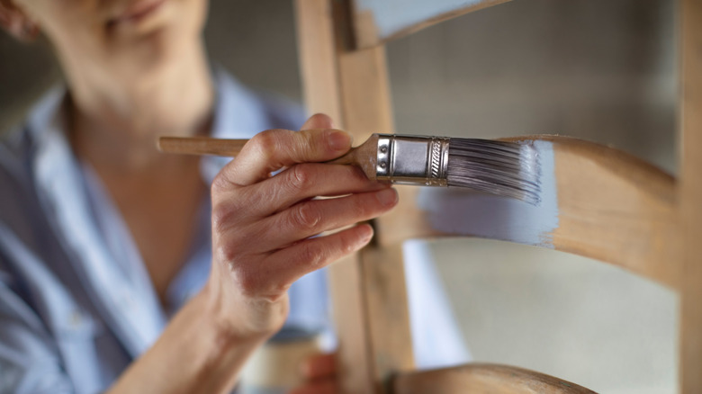 A woman painting a pine chair with grey paint.