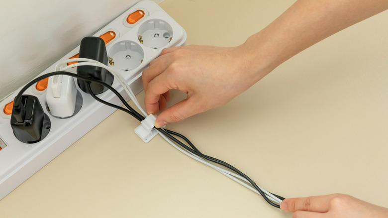 An extension cable with various plugs and a hand tying them together with a cable tie.