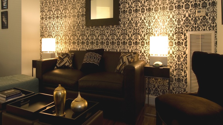 A living room with a feature wallpaper wall in a brown patter with brown sofa and armchair in front.