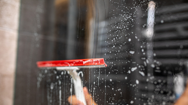 A hand uses a squeegee to wipe down shower glass