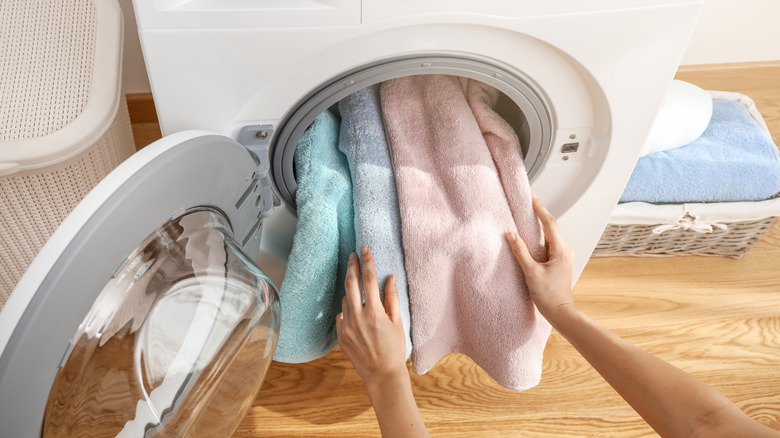 A person loads blue and pink bath towels into a washing machine
