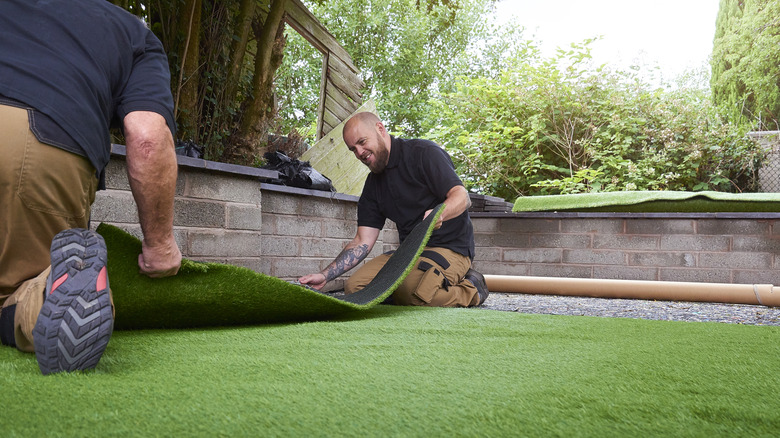 Two workers place artificial turf