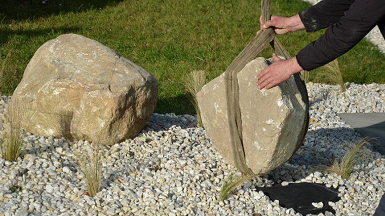 A person lowers a boulder into a garden