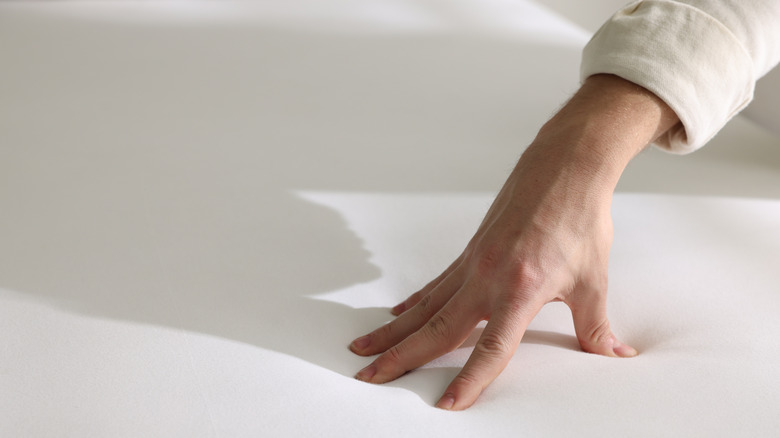 A hand testing the firmness of a memory foam mattress.