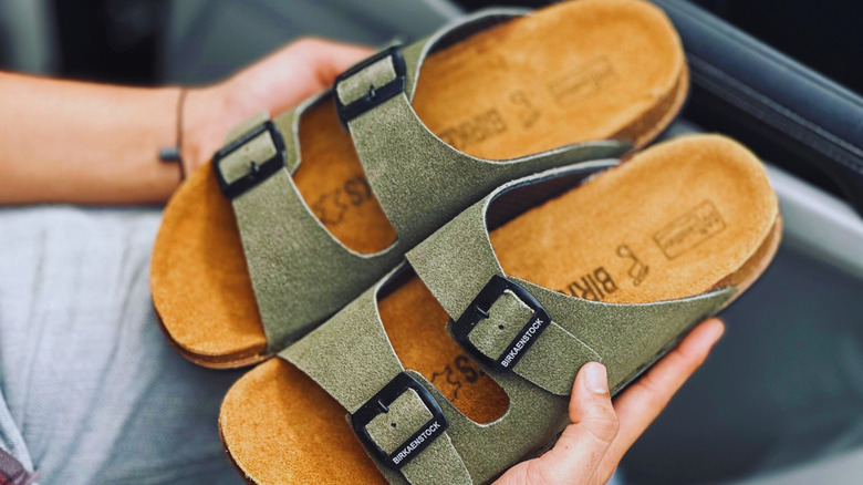 A man holding a pair of Birkenstock sandals in green.