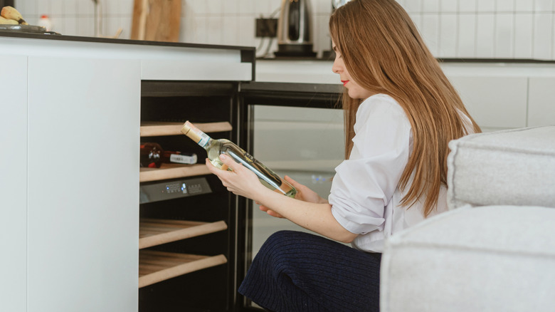 A woman storing a bottle of wine in a wine cellar in her kitchen.