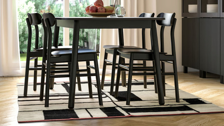 A black and white patterned flat rug with red trim sitting under a black dining table
