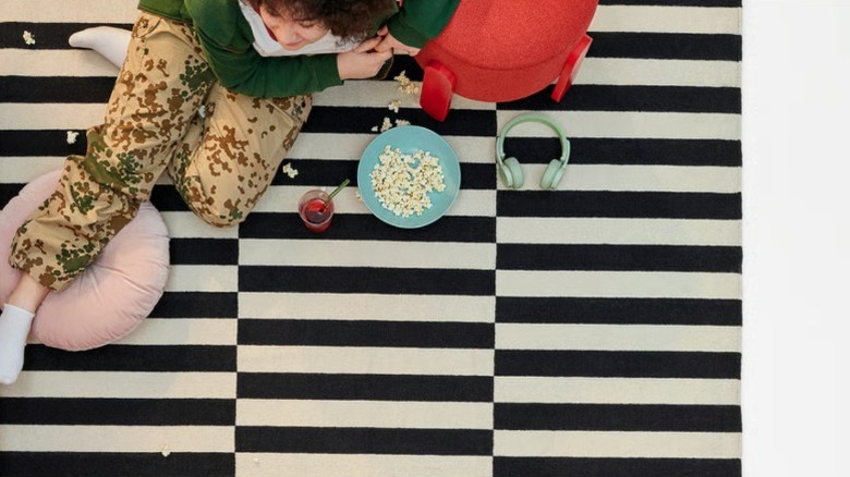 A girl sitting on a black and white striped woven rug eating popcorn