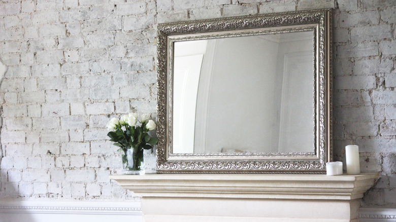Ornate mirror sitting on a mantle against a brick wall