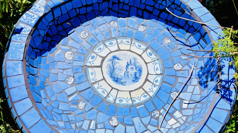 Mosaic bird bath primarily made from broken china in shades of blue.