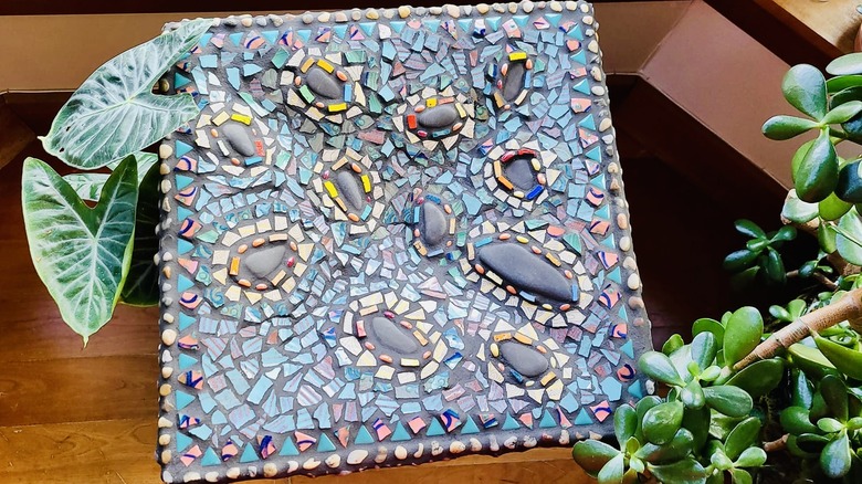 Mosaic bird bath in a square shape with broken china and stones.