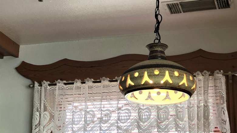 A brown 1970s light fixture made from metal hanging in a dated kitchen.