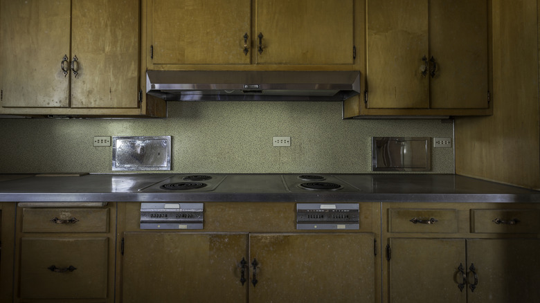 A dark, drab 1970s kitchen with wood laminate cabinets and stainless steel counters.