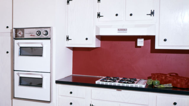 A 1970s kitchen with lots of upper cabinets painted white.