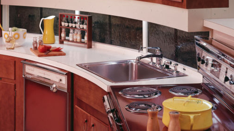 A 1970s kitchen with Formica countertops and a stainless steel corner sink.