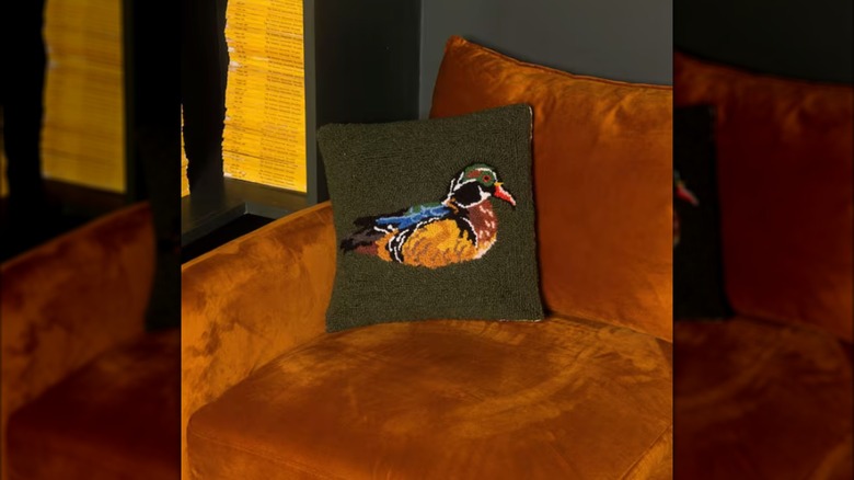 The Wood Duck Green Throw Pillow from Makers Collective on a brown upholstered sofa