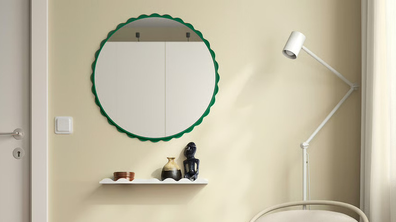 IKEA DAGGKAPRIFOL Mirror hung on a wall with a shelf down below and furniture in the foreground