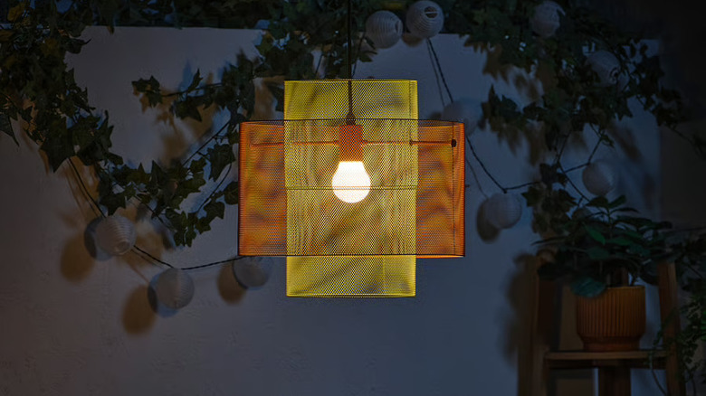 The SOLVINDEN ceiling lamp hung in a patio area outside at night with plants in the background