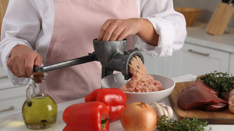 A woman mincing meat with an old hand-cranked meat grinder