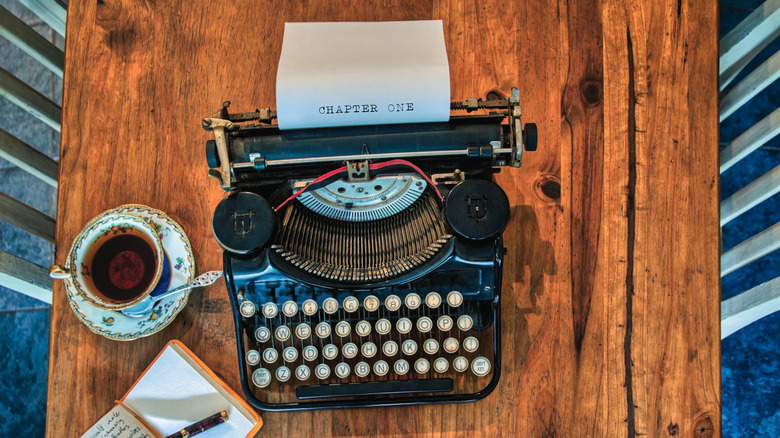 An old typewriter on a table with a cup of tea and a notepad