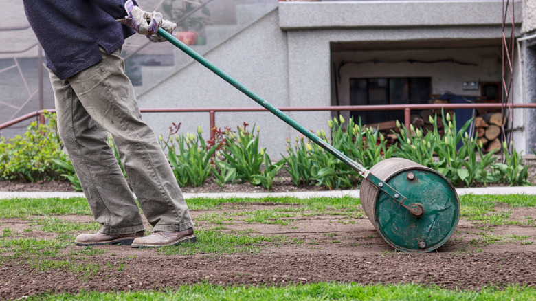 A man pulling a heavy roller over his lawn