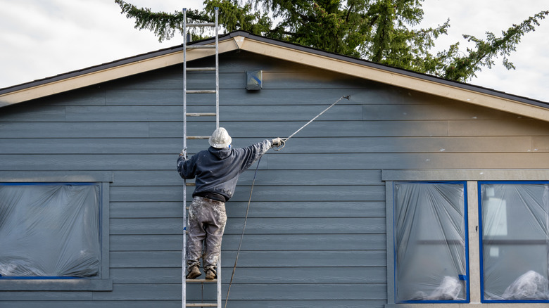 man painting siding on a house