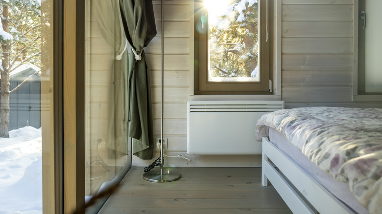 A wall-mounted electric heater in a bedroom with a view of snow outside