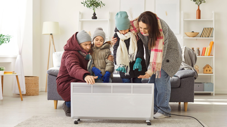 A cold family dressed in warm outdoor clothes gathering around a broken electric radiator