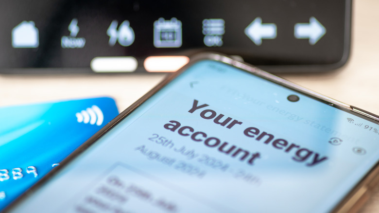 A smartphone display showing a home's energy account with a smart meter in the background