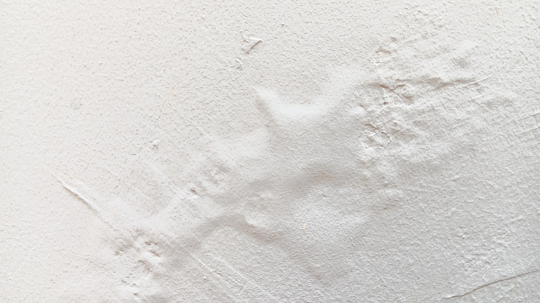 A white textured wall with a bubble in the paint