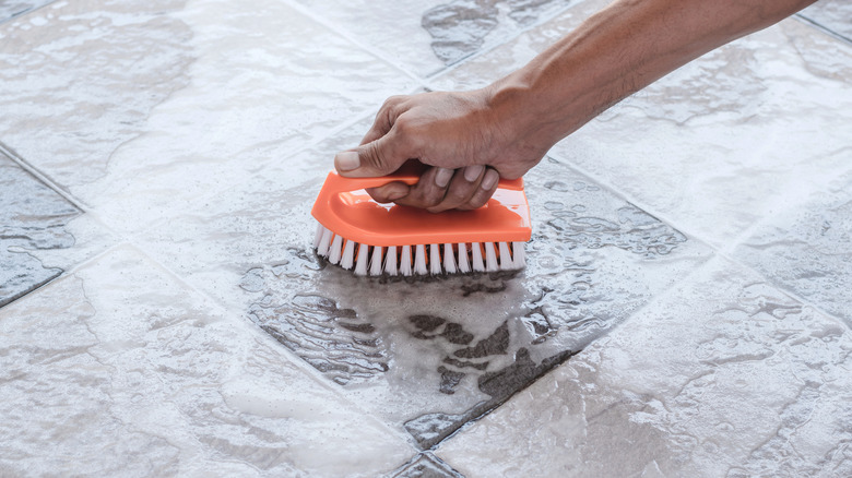 Person scrubbing a tile floor with an orange scrub brush