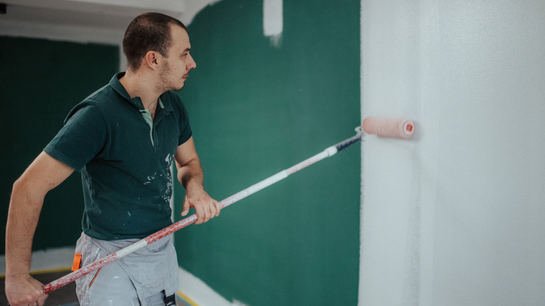 A man painting an interior wall with a roller