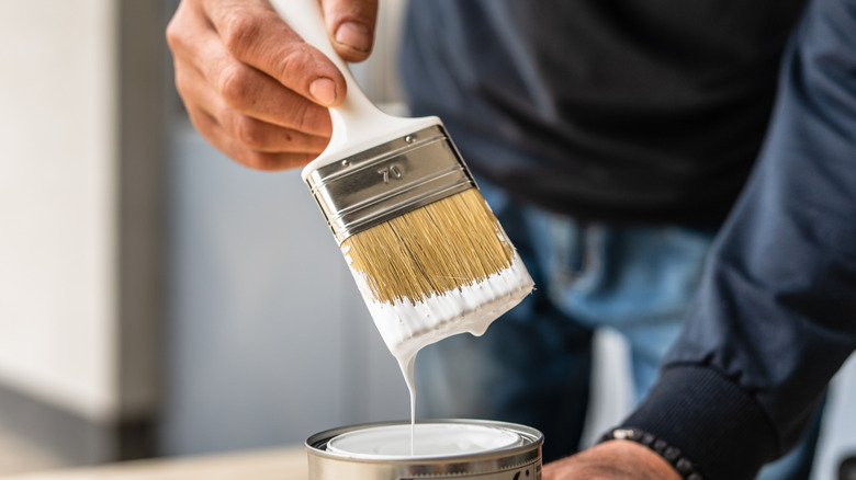 A person dipping a paint brush in a paint can