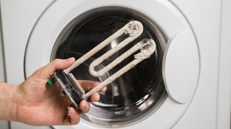 A person holding a mineral-covered heating element in front of a washing machine