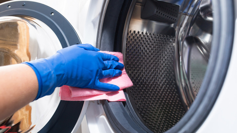 Close-up of a blue-gloved hand cleaning a washing machine
