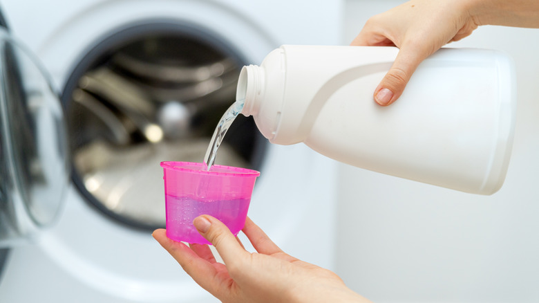 A person adding bleach to a cup in front of a washing machine