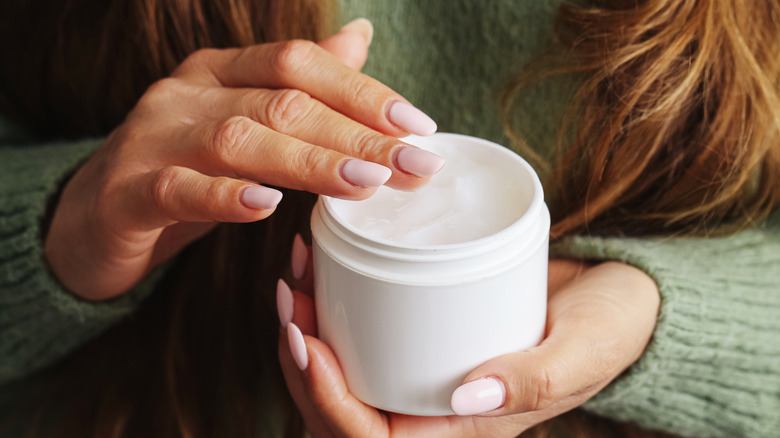 Close-up of a hand holding a pot of body cream or butter