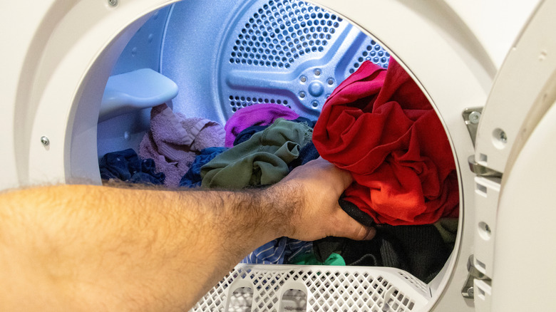 A hand reaching into a dryer with mixed laundry, including clothes and towels