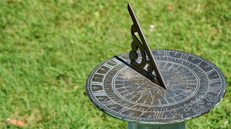 A vintage metal sundial in front of grass.