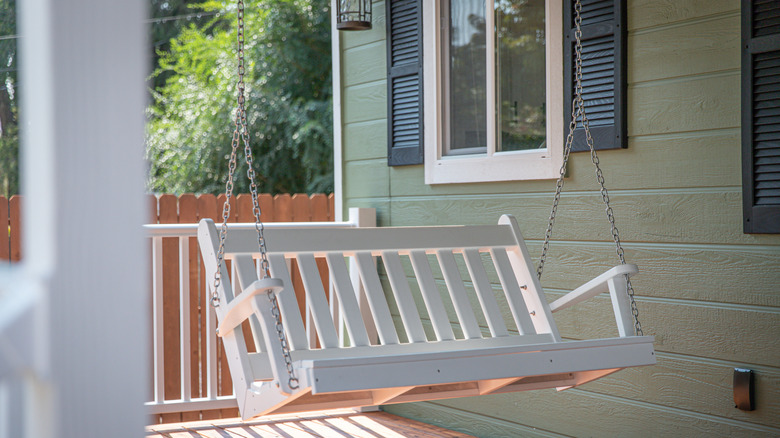 A white porch swing in front of a green house.