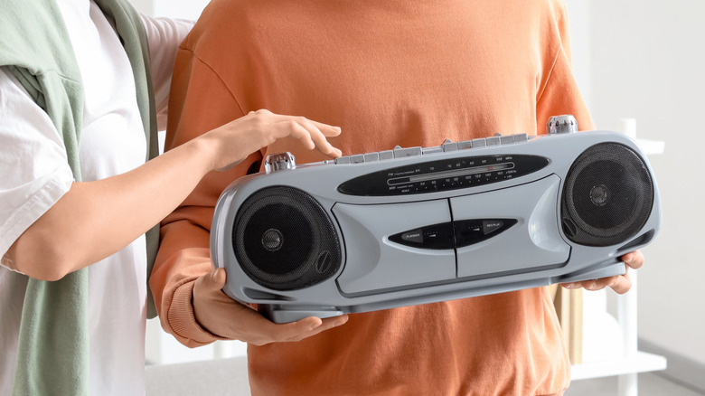 A hand presses a button on a vintage boombox.