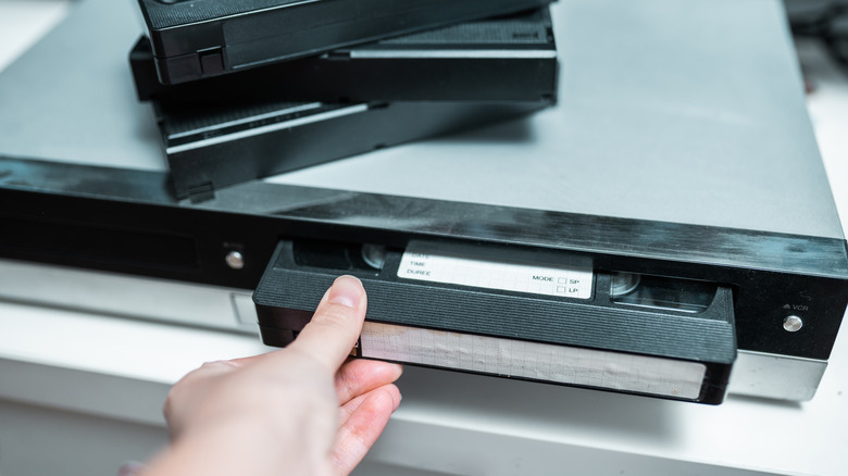A hand inserting a VHS tape into a VCR.