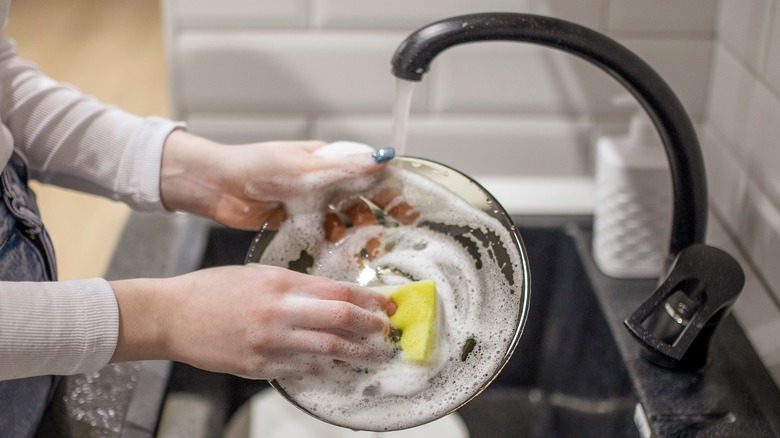 Person washing glass bowl under faucet